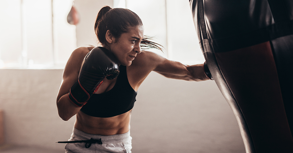 Athlete in boxing gloves punching a heavy bag in a gym