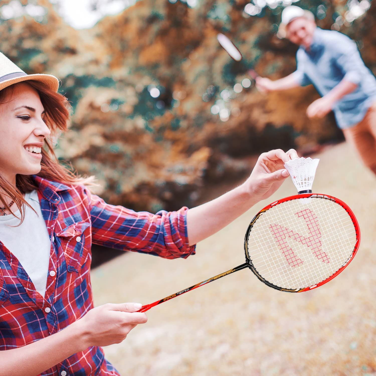 Two people playing badminton in a garden, one about to serve a shuttlecock